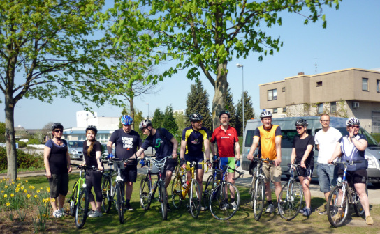 10 Mitarbeiter in bunten Fahrradtrikots mit Ihren Rädern vor dem ersten Training.