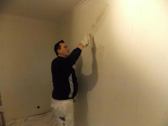 Ein Maler spachtelt eine Wand.