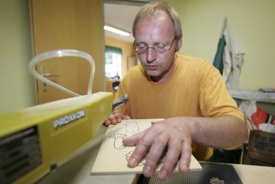 ein Mitarbeiter sägt Holzteile für einen Hampelmann an der Dekupiersäge aus