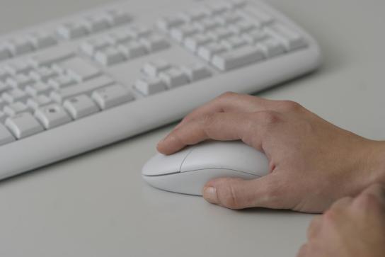 eine Hand auf einer Maus neben einer Tastatur
