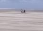 Drei Personen gehen bei Sturm über den Strand 